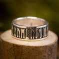 Indlæs billede i Gallery viewer, Sølvring Uovervindelig 925s Sølv, en sølvring med indviklede futhark-runer, hviler på en tekstureret træoverflade, sat mod en sløret grøn baggrund. Ringens indgraveringer, lavet af ægte sølv, består af ældgammelt udseende symboler, der omslutter hele båndet.