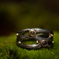 Indlæs billede i Gallery viewer, Et nærbillede af unikke håndlavede smykker hvilende på en seng af mos. Den håndlavede fingerring - Eryn Design - Moria (Med sten) har et mørkt, tekstureret bånd med organiske, grenlignende designs udsmykket med små 14 karat guldkugler og tre cabochon ædelstene, inklusive ametyst. Baggrunden er blødt sløret, hvilket understreger ringens detaljer.