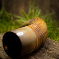 Indlæs billede i Gallery viewer, Et nærbillede af et langt, buet, rustent metalrør liggende på en træoverflade med græs i baggrunden. Piben har et tekstureret mønster, muligvis på grund af korrosion, der minder om en gammel Drikkehorn Chief dekoration fra Vikingemarked. Det ser ud til at være en antik genstand.