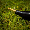 Indlæs billede i Gallery viewer, En poleret Drikkehornulv ligger på grønt græs. Det let buede, vintage sorte og guld horn har en skinnende sort krop og et guld ornamentalt mundstykke. Nærbilledet fremhæver græssets tekstur og hornets håndværk – perfekt til vikingemarkeder.