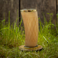 Indlæs billede i Gallery viewer, Et "Drikkeglas Horn med mønster" (300ml) med guldkant og diamantformede graveringer, fyldt med en brun væske, står på en træskranke midt i højt grønt græs med en sløret træbaggrund.