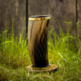 Indlæs billede i Gallery viewer, Et højt, indviklet designet Drikkeglas Horn med mønster (300 ml) med en gylden kant, placeret på en træskranke, er placeret på levende grønt græs. Baggrunden har en rustik trævæg.