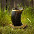 Indlæs billede i Gallery viewer, Drikkeglas Horn med Mønster (100 ml), med en guldkantet kant, står oprejst på en træbund. Hornet har et indviklet mønster på kryds og tværs og vises på en græsklædt udendørs overflade med en sløret baggrund af frodigt grønt og træhegn.