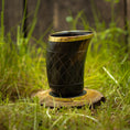 Indlæs billede i Gallery viewer, Et dekorativt Drikkeglas Horn med Mønster (100ml) med guldkant står på en træskive placeret på grønt græs. Skålen har et indviklet udskåret mønster og har en poleret finish, hvilket skaber et rustikt og naturligt udseende. Baggrunden er let sløret og fokuserer opmærksomheden på koppen.