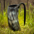 Indlæs billede i Gallery viewer, Et Vikingekrus Nature Horn (600-800ml) med et håndtag, prydet i et marmoreret sort og gråt mønster, står oprejst på græsklædt terræn med en træbaggrund. Dette stykke legemliggør essensen af vikingekrus, der forener tradition og håndværk.
