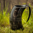 Indlæs billede i Gallery viewer, Et poleret sort Vikingekrus Helleristning Horn (600-800ml) med to dekorative bånd vises oprejst på græs med en træbaggrund. Håndlavede hornkrus har et håndtag, der giver den et kruslignende udseende.