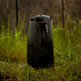 Indlæs billede i Gallery viewer, Et Vikingekrus Thors Hammer Horn (600-800 ml) med et indgraveret design, der ligner Thors Hammer, hviler på en plet græs, med en forvitret trævæg i baggrunden.