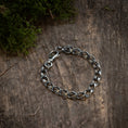 Indlæs billede i Gallery viewer, Armbånd Chainlinked 5mm 925s Sølv, lavet af oxideret 925s Sterling sølv, ligger på en forvitret træoverflade. Noget grønt mos er synligt i det øverste venstre hjørne af billedet, hvilket tilføjer et naturligt touch til den rustikke baggrund og fremhæver denne unisex-smykkes rå elegance.