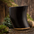 Indlæs billede i Gallery viewer, Drikkeglas Horn Plain (500 ml) står elegant oprejst på en tekstureret træoverflade og viser dets glatte, buede sorte bøffelhorn med en solbrun base. Baggrunden inkluderer træstykker og pletter af grønt mos, der bidrager til scenens rustikke og naturlige stemning.