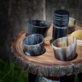 Indlæs billede i Gallery viewer, En rustik "Holder til vin med horn" med fem små hornkopper og en sort flaske står på en sløret, jordagtig baggrund. Bakkens naturlige tekstur og jordfarver fremhæver æstetikken, hvilket gør den perfekt til servere drikkevarer.