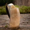 Indlæs billede i Gallery viewer, En Mini Vikingekrus Horn Thors Hammer (100 ml) sidder på en tekstureret stenoverflade, dens udsmykkede hornformede design minder om vikinge-drikkekar. Med et indgraveret cirkulært mønster med indviklede detaljer, muligvis forestillende et middelalder- eller fantasiemblem, kunne det nemt fremvises i Roskilde showroom. Baggrunden er sløret grønt og murværk.