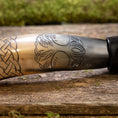 Indlæs billede i Gallery viewer, Nærbillede af Drikkehorn Yggdrasil med Mønster, der viser dens polerede overflade prydet med indviklede udskæringer. Designet har et sammenflettet knudemønster til venstre, der går over til et træmotiv med detaljerede blade i midten og til højre. Hornet hviler på en rustik træholder, der minder om vikingemarkeder.