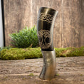 Indlæs billede i Gallery viewer, Drikkehorn Yggdrasil med Mønster, en poleret hornkar, der minder om traditionelle drikkehorn, hviler på en træoverflade med mos og grønt i baggrunden. Denne udsøgt udformede tankard byder på indviklede graveringer og et detaljeret design af et træ med indvævede grene og rødder - perfekt til naturentusiaster eller vikingemarkeder aficionados.