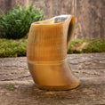 Indlæs billede i Gallery viewer, Et nærbillede af Vikingekrus Bark Horn (600-800ml) sat på en rustik træoverflade med grønt mos og planter i baggrunden. Ølkrusen viser en jævn gradient fra lys til mørk og har lodrette riller langs den øverste halvdel.
