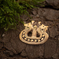 Indlæs billede i Gallery viewer, Et Broche Vikingeskib Bronze med indviklede designs af to stiliserede hestehoveder og et centralt kranium hviler på en revnet, jordagtig overflade. Grønt mos er synligt i venstre side af billedet. Brochen fremkalder udseendet af en middelalderlig eller gammel vikingetiden-artefakt.
