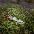 Indlæs billede i Gallery viewer, Broche Rose med Rav 925s Sølv, en sølvfarvet broche formet som en stilk med blade, holder autentisk rav, der ligner en blomsterknop, og hviler på levende grønt mos. Det detaljerede håndværk af denne romantiske gave efterligner en naturlig rose.
