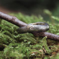 Indlæs billede i Gallery viewer, En rustik, naturinspireret ring på en mosbevokset overflade. Ringen, kendt som Fingerring - Eryn Design - Branches, har en trætekstur og en lille indlejret diamant, der fremkalder en naturlig, jordagtig æstetik. Den fremviser dansk design, den sidder fint på en kvist og blander sig problemfrit med omgivelserne.
