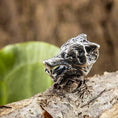 Indlæs billede i Gallery viewer, Et nærbillede af en detaljeret Skægperler / Hårpynt Ulv 925s Sølv-ring, der forestiller et ulvehoved, hvilende på et stykke træ med sløret grønt løv i baggrunden. Det indviklede design fanger ulvens vilde og voldsomme udtryk.
