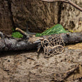 Indlæs billede i Gallery viewer, En Broche Urnesstil Bronze hviler på et stykke forvitret træ, omgivet af tekstureret bark og grønne blade i baggrunden. Lys giver subtil vægt på de indviklede detaljer i dets autentiske bronzemønster.
