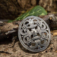 Indlæs billede i Gallery viewer, Broche Borrestil 925s Sterling Sølv, prydet med et delikat og komplekst keltisk knudedesign, er elegant udstillet på et stykke bark. Sammensætningen forstærkes af et grønt blad i baggrunden, der bidrager til den naturlige stemning. De omgivende rustikke omgivelser fremhæver brochens indviklede tekstur og overlegne håndværk, hvilket gør den til et lokkende stykke for enhver historieinteresseret.
