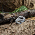 Indlæs billede i Gallery viewer, En detaljeret Broche Midgårdsormen 925s Sterling Sølv med en sammenflettet, tekstureret knude er placeret på en ru bark. Grønne blade giver en naturlig baggrund, der forstærker den rustikke og jordiske æstetik ved dette Vikingetiden-symbol.
