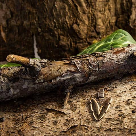 En møl camoufleret mod en trægren sidder på barkens ru overflade, der ligner en gammel Pilespids Vedhæng Bronze fra vikingetiden. Mølens vinger og mønstre blander sig problemfrit med træets teksturer og farver, mens et grønt blad er synligt i baggrunden.