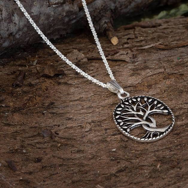 En smuk Halskæde Margherita 925s Sterling Sølv 1,5 mm med et detaljeret trædesign ligger på en tekstureret træoverflade. Sølvvedhænget er cirkulært med en indviklet, stiliseret afbildning af et træ med forgrenede lemmer og rødder, smukt ophængt i den fint udformede Margherita-kæde.