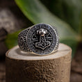 Indlæs billede i Gallery viewer, Sølvring Thors Hammer 925s Sølv-ringen viser stolt et detaljeret Mjölnir (Thors Hammer)-emblem i midten, omgivet af indviklede runer og mønstre. 925 Sterling sølv ringen hviler på en struktureret stensokkel med en sløret grøn bladagtig baggrund.
