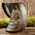 Indlæs billede i Gallery viewer, Et poleret, buet Vikingekrus Yggdrasil-horn (600-800 ml) med et håndtag, med en indviklet hvid indgravering af et symmetrisk, keltisk-inspireret design. Drikkehornskoppen er sat på en rustik træbaggrund med grønt mos og en forvitret træoverflade.
