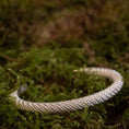 Indlæs billede i Gallery viewer, Et Armbånd Armbånd Empor 925s Sterling Sølv, et fantastisk sølvflettet armbånd, ligger på en seng af levende grønt mos. Det indviklede design står i kontrast til den naturlige, frodige baggrund, hvilket understreger dets detaljerede håndværk.
