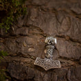 Indlæs billede i Gallery viewer, En detaljeret Thors Hammer Vedhæng 925s Sterling sølv Celtic hviler på bark med ru tekstur. Vedhænget er lavet af massivt 925s sølv og har indviklede nordiske designs og keltiske mønstre, omgivet af pletter af grønt mos, hvilket skaber en naturlig og jordnær stemning.
