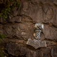 Indlæs billede i Gallery viewer, Thors Hammer Vedhæng 925s Sterling sølv Celtic, et sølvvedhæng designet til at ligne Mjolnir (Thors hammer), har indviklede nordiske og keltiske mønstre. Den fint udformede 925 sterling sølv hammer vises mod en struktureret træbark baggrund, med mos rundt om kanterne, der tilføjer et naturligt præg til billedet.
