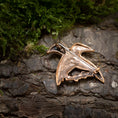 Indlæs billede i Gallery viewer, En lille, indviklet designet Broche Hugin og Munin Bronze i form af en fugl hviler på en struktureret træbarkoverflade med grønt og mos i baggrunden.
