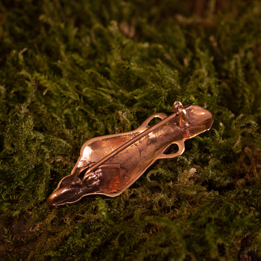 En Broche Hugin / Munin Bronze med et indviklet design ligger på en bund af grønt mos. Mosen giver en naturlig og struktureret baggrund, der står i kontrast til brochens skinnende bronzeoverflade, hvilket fremkalder fortællinger om Odins æra.