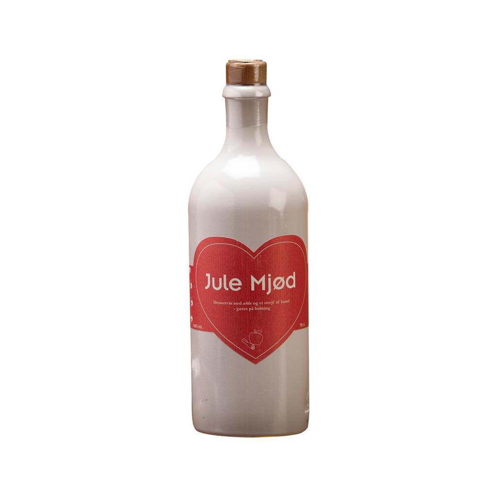 En Dansk Mjød Julemjød (70cl) flaske har et hvidt keramisk ydre prydet med en rød hjerteformet etiket med inskriptionen "Julemjød" i hvid tekst. Denne elegante flaske er toppet med en propprop og har et enkelt, raffineret design, hvilket gør den perfekt til at nyde som en udsøgt dessertvin.