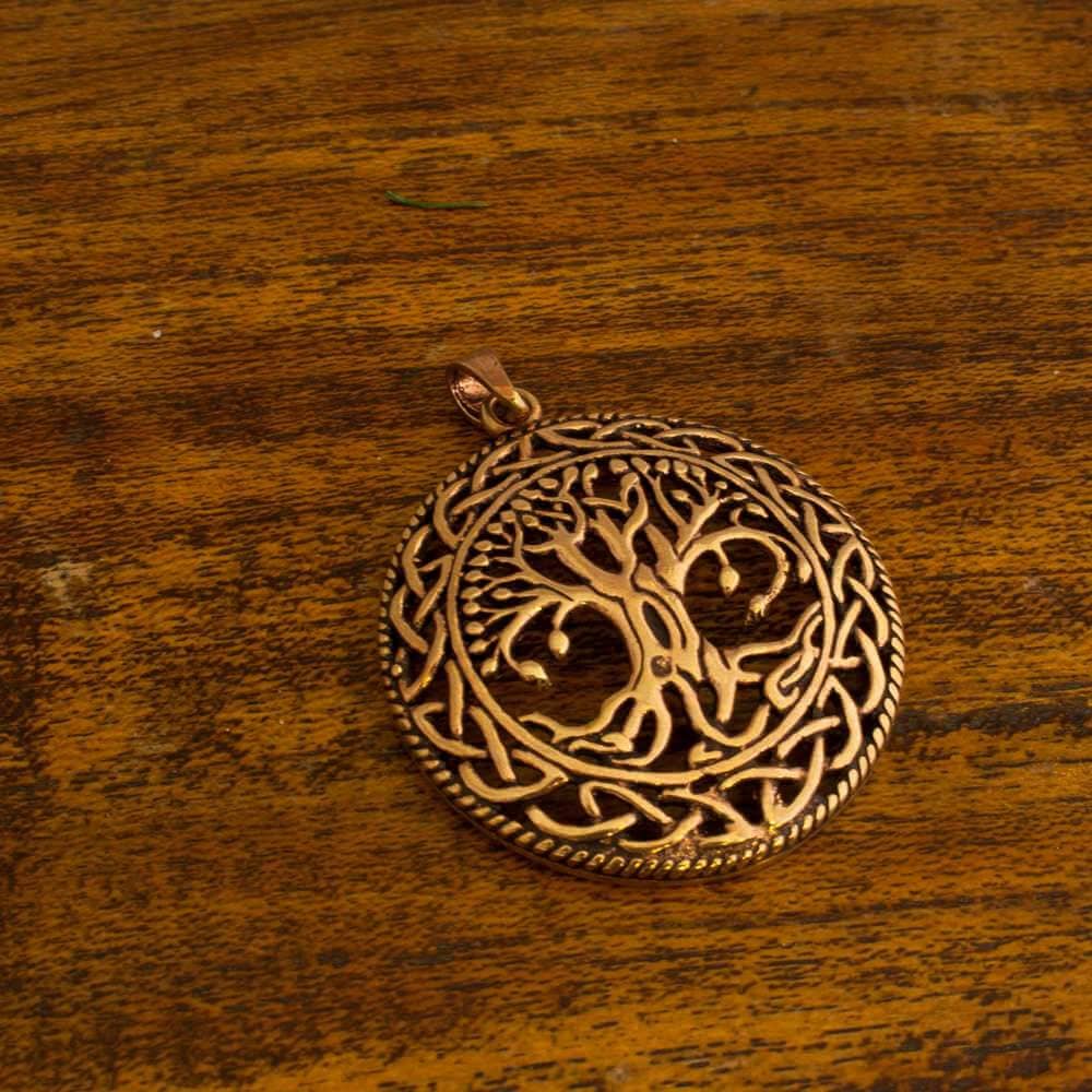 En indviklet designet Yggdrasil Livets Træ Vedhæng Runth Bronze ligger på en træoverflade. Vedhænget er bronze og ovalt, med træet i midten omgivet af detaljerede keltiske knuder langs kanten. Træbaggrunden har et rustikt, tekstureret udseende.